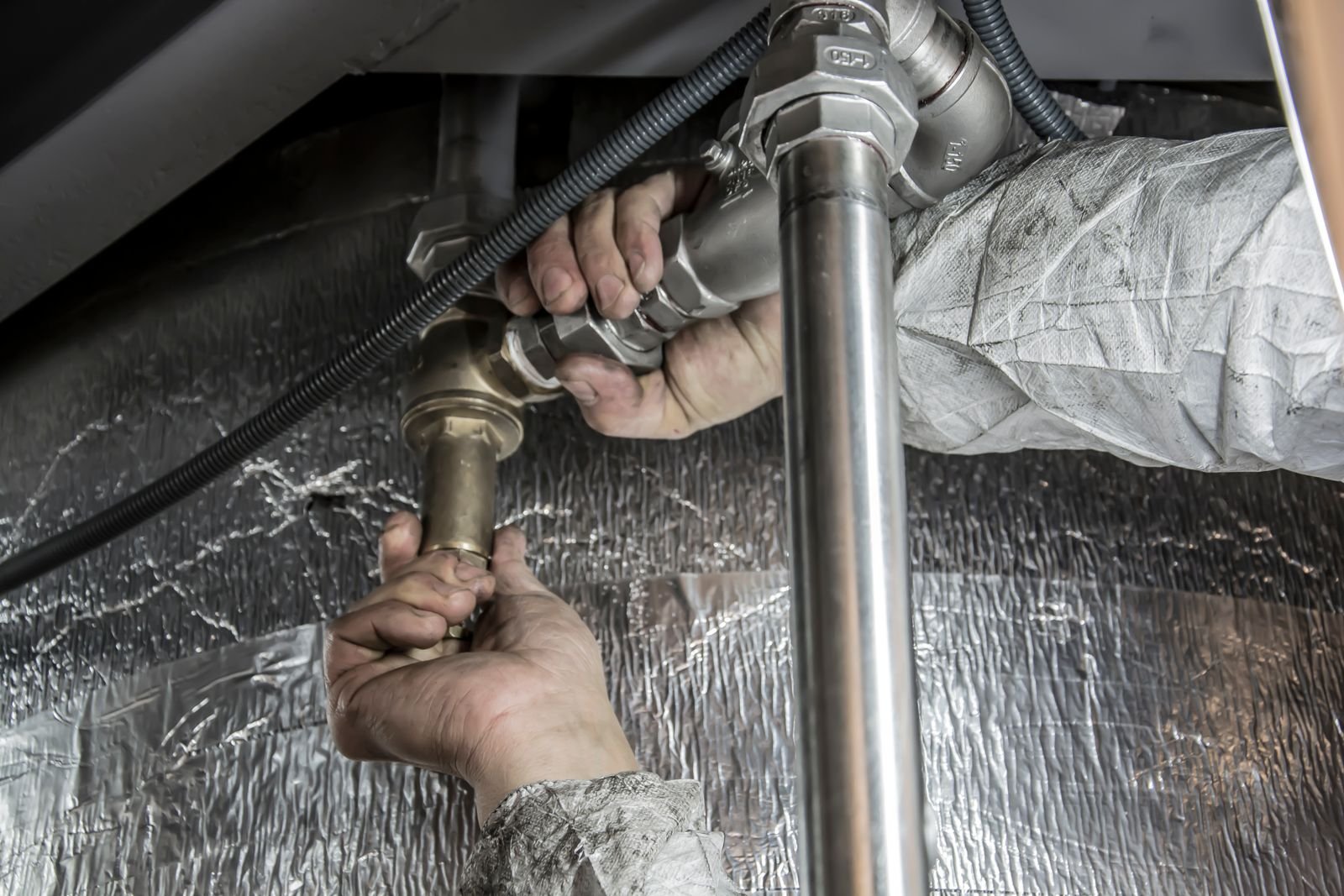 Close-up of hands repairing a supply line fitting under a fixture after a pipe failure